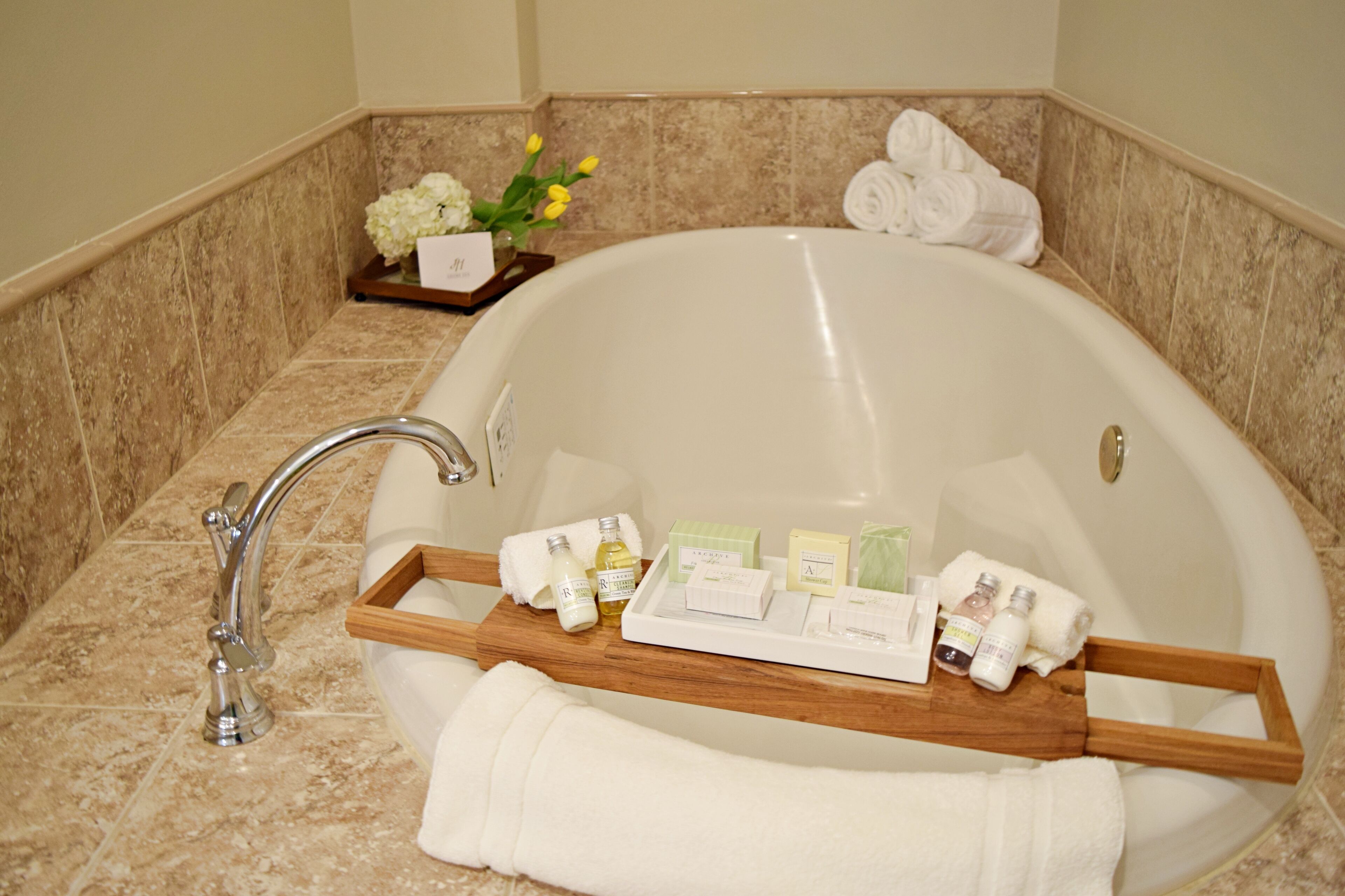 A bathroom with a bathtub, a wooden tray with toiletries, and towels.