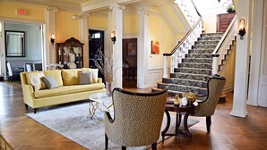 A spacious lobby with a yellow sofa, patterned chairs, a staircase, and a dining area. - JH Adams Inn, Trademark Collection by Wyndham (High Point)