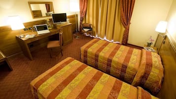 Une chambre d’hôtel avec deux lits, un bureau avec un ordinateur portable, une chaise et une petite table avec une lampe.
