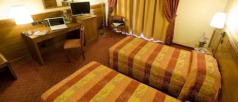 A hotel room with two beds, a desk with a laptop, a chair, and a small table with a lamp.