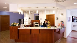 A reception area with a wooden counter, a printer, and a vase of flowers. - Hotel Master (Turin)