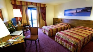 A hotel room with two beds, a desk with a laptop, a chair, and a window with curtains. - Hotel Master (Turin)