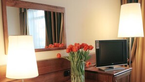 A hotel room with a wooden dresser, a television, a mirror, and a vase of red tulips. - Hotel Master (Turin)