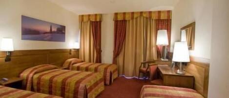 Una habitación de hotel con cuatro camas individuales, un ventanal con cortinas, un cuadro en la pared y dos lámparas de noche.