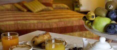A breakfast tray with coffee, juice, pastries, and a fruit bowl on a table in a hotel room.