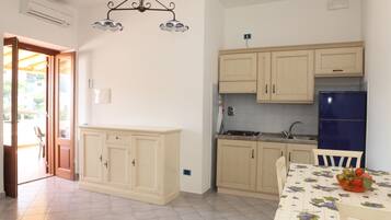 A kitchen with light wooden cabinets, a blue refrigerator, and a dining table with a fruit bowl.