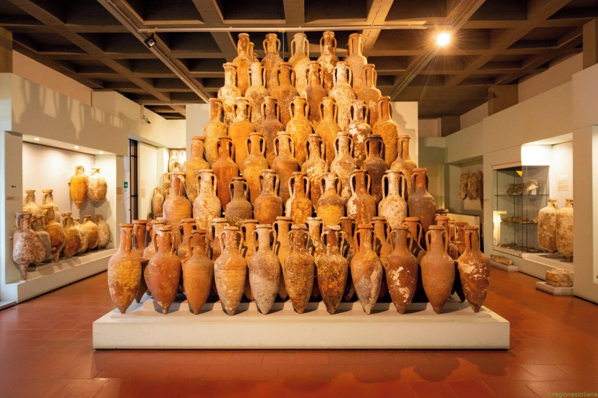 A display of ancient pottery arranged in a pyramid-like structure in a museum.