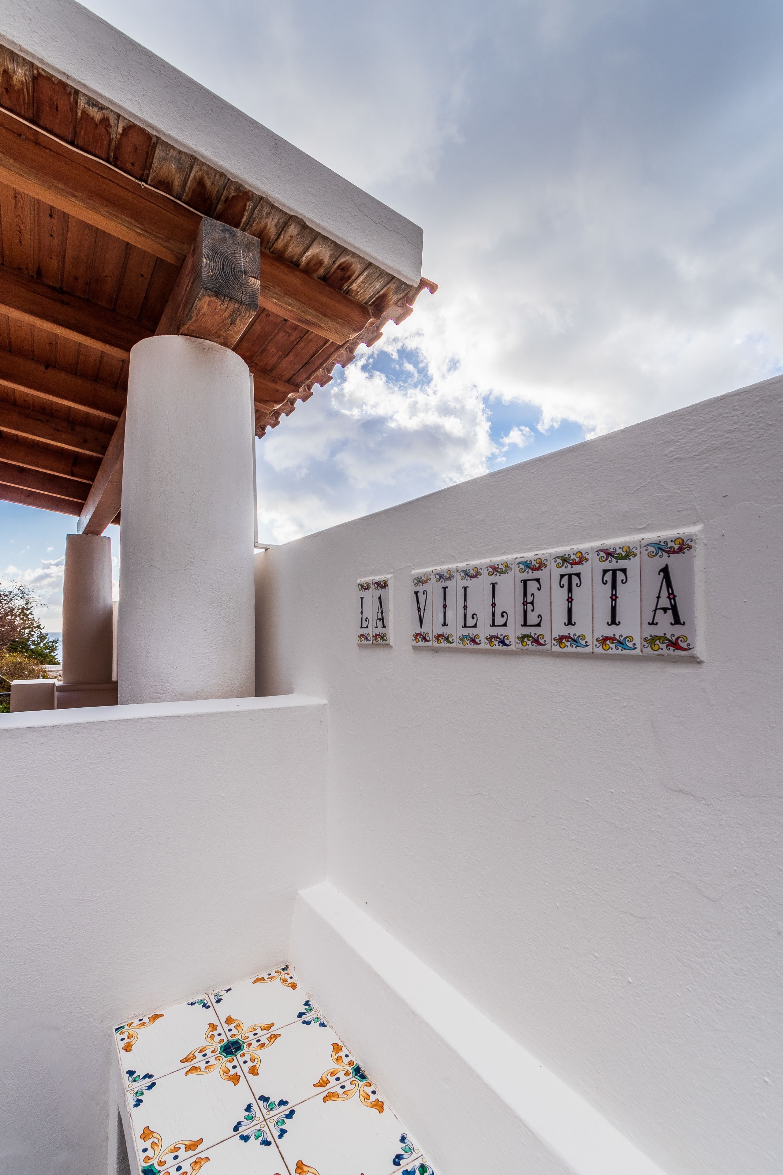 A white wall with the name "LA VILETA" in decorative tiles, a wooden pergola, and a tiled table with floral patterns.