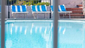 Una piscina con tres sillones reclinables azul y blanco y un muro de piedra al fondo.