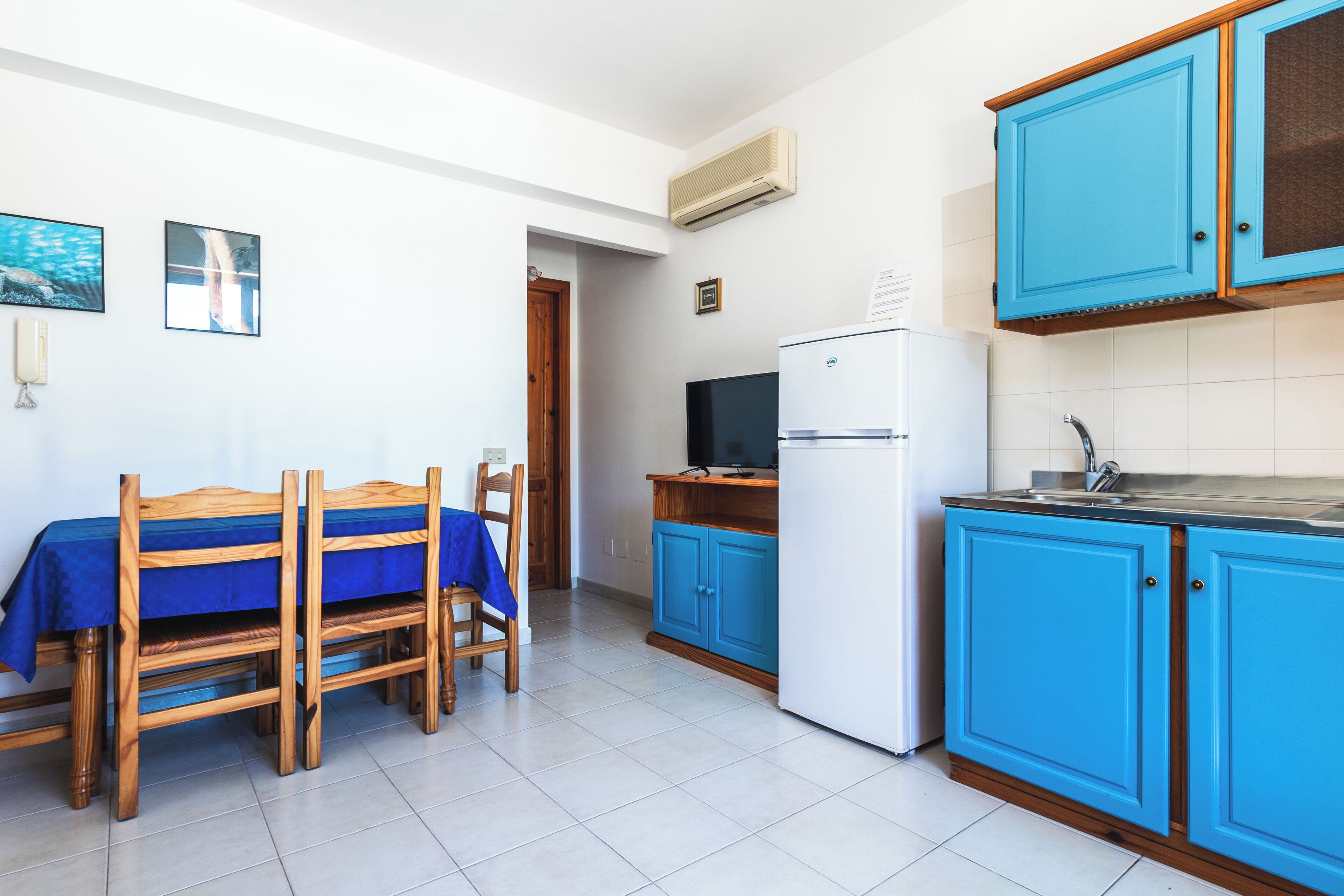 A kitchen with blue cabinets, a white refrigerator, and a dining table with chairs.