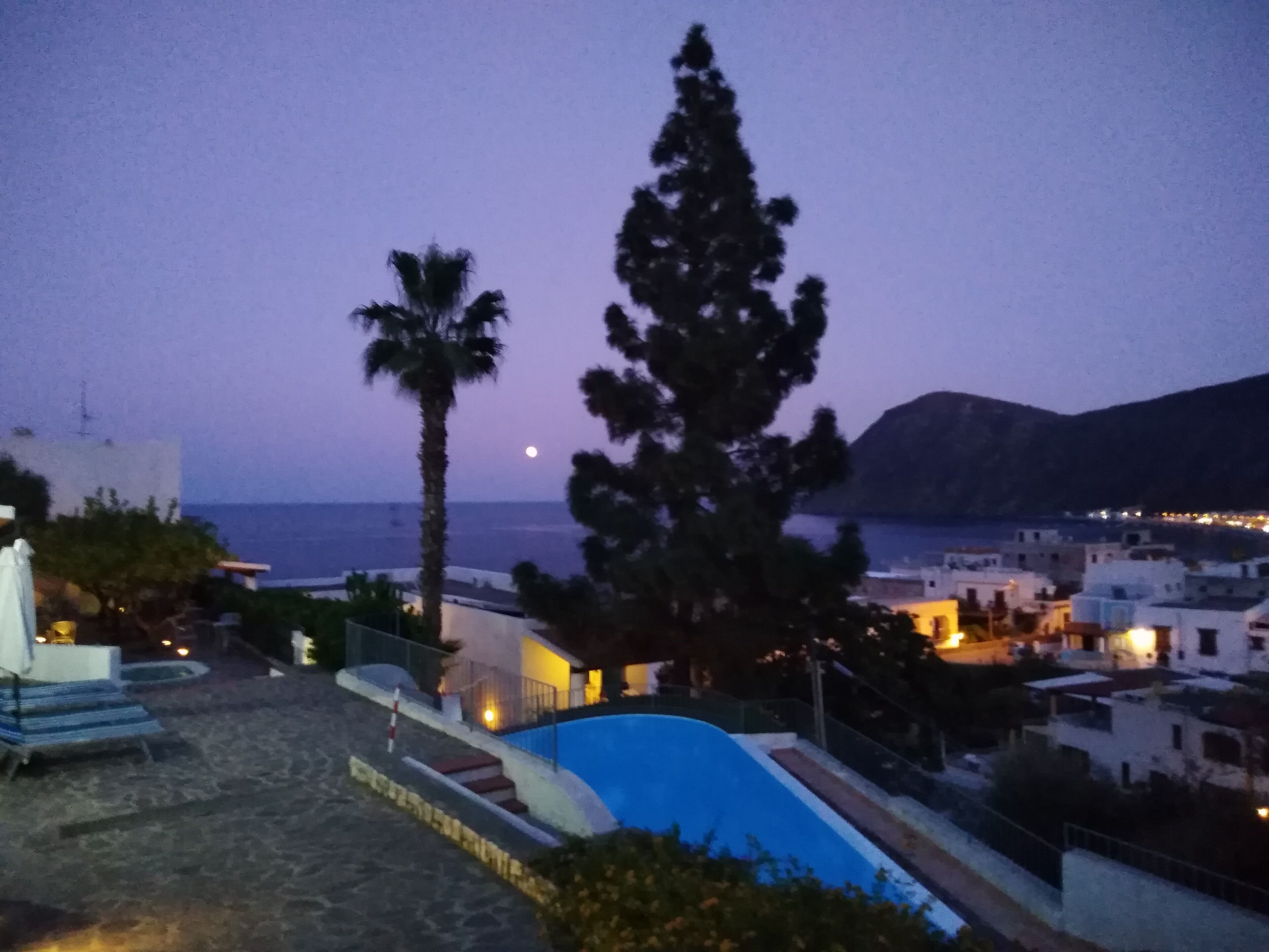 A coastal view with a pool, palm trees, and a sunset.