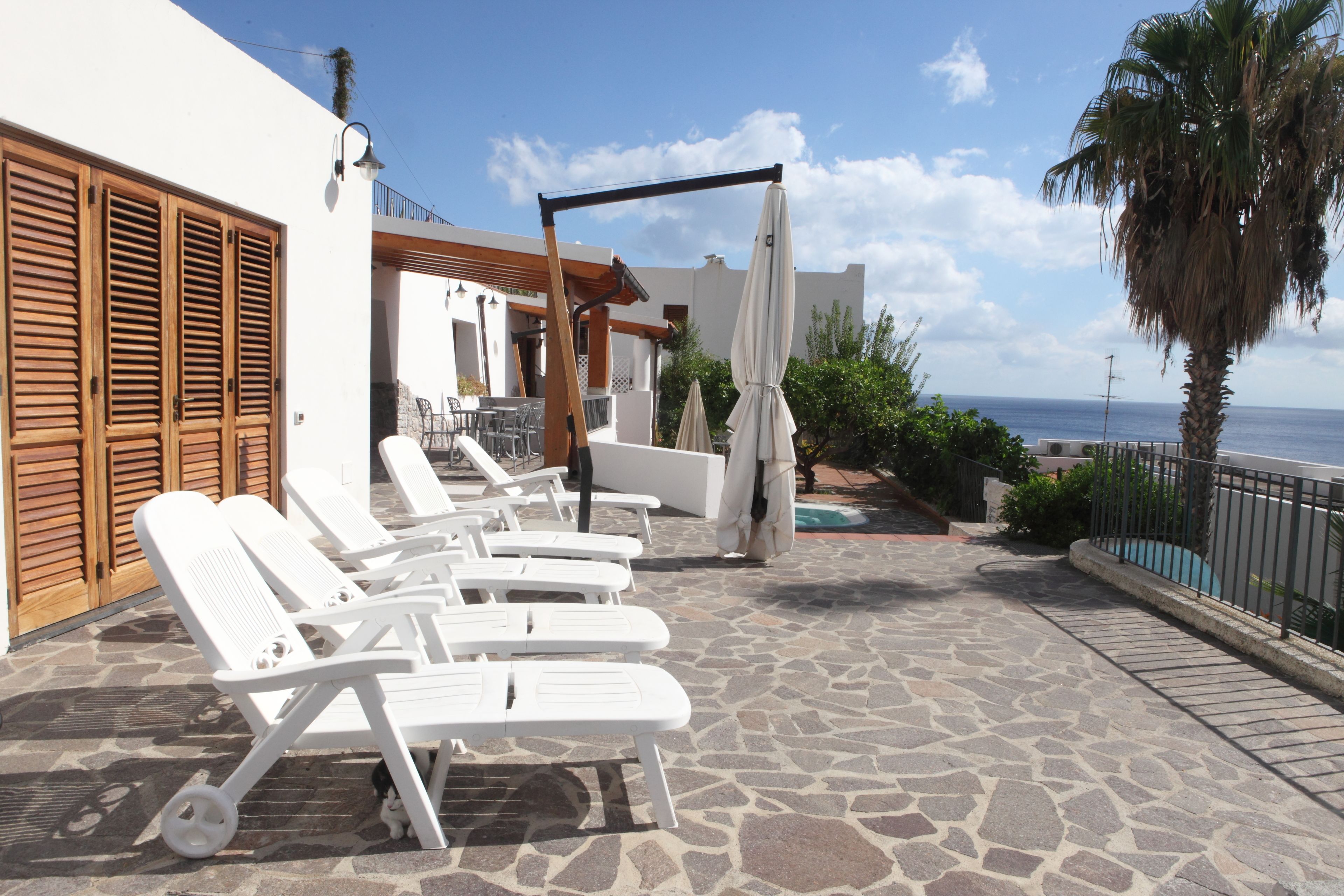 A patio with white lounge chairs, a pergola, and a view of the ocean.