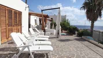 A patio with white lounge chairs, a pergola, and a view of the ocean.