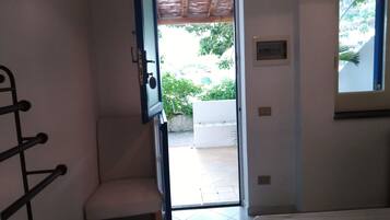 Une pièce comprenant un lit, une chaise, une fenêtre et une porte donnant sur un espace extérieur agrémenté de plantes.