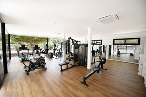 Un gimnasio amplio con diversos equipos de ejercicio, ventanas grandes y piso de madera.