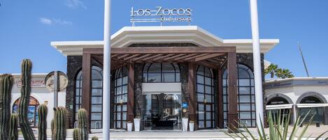 The exterior of Los Zocos Club Resort with a covered entrance, large windows, and cacti in the foreground.