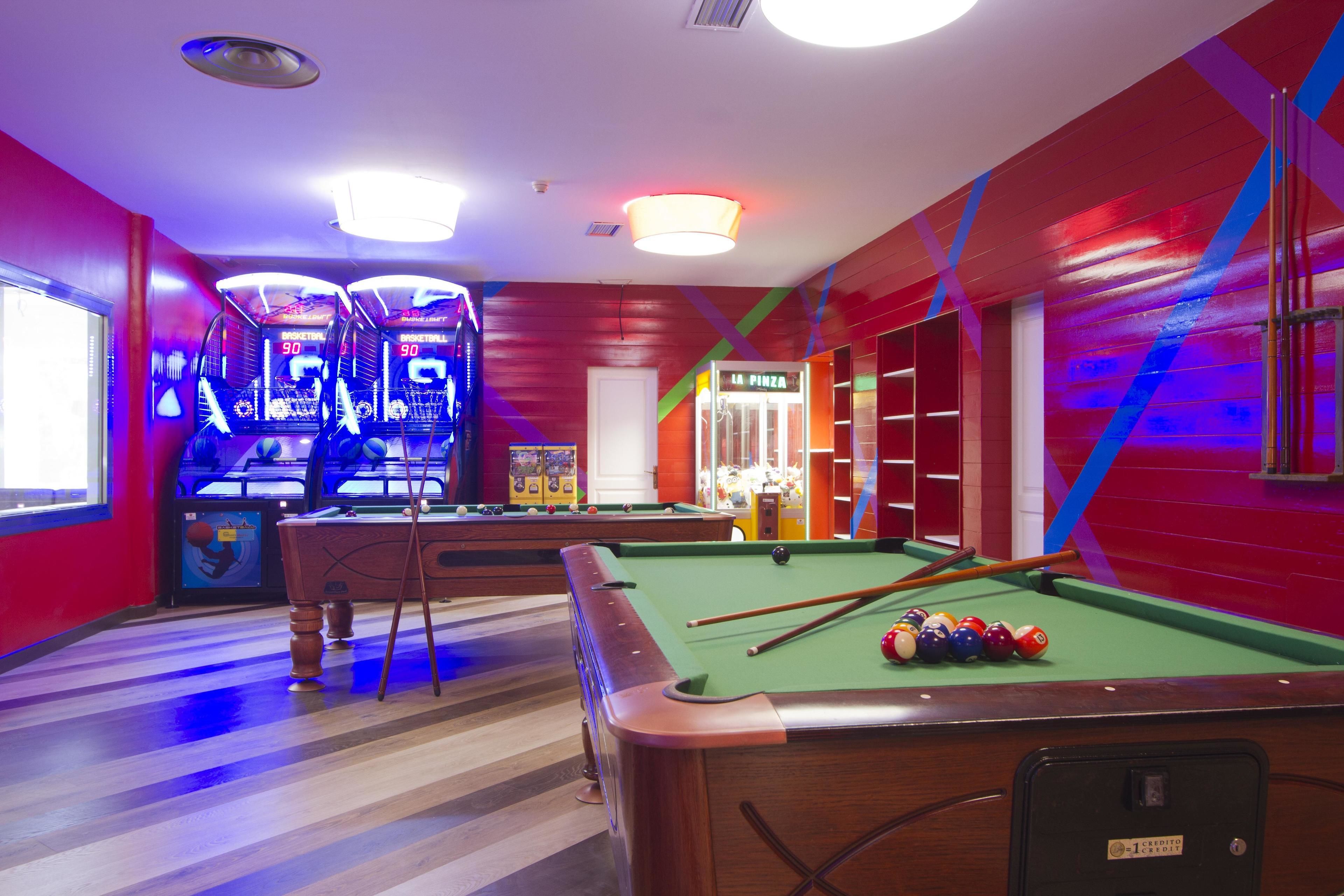 Una mesa de billar con bolas, un portaobjetos de billar y una máquina de pinball en una habitación con paredes rojas y suelo a rayas.