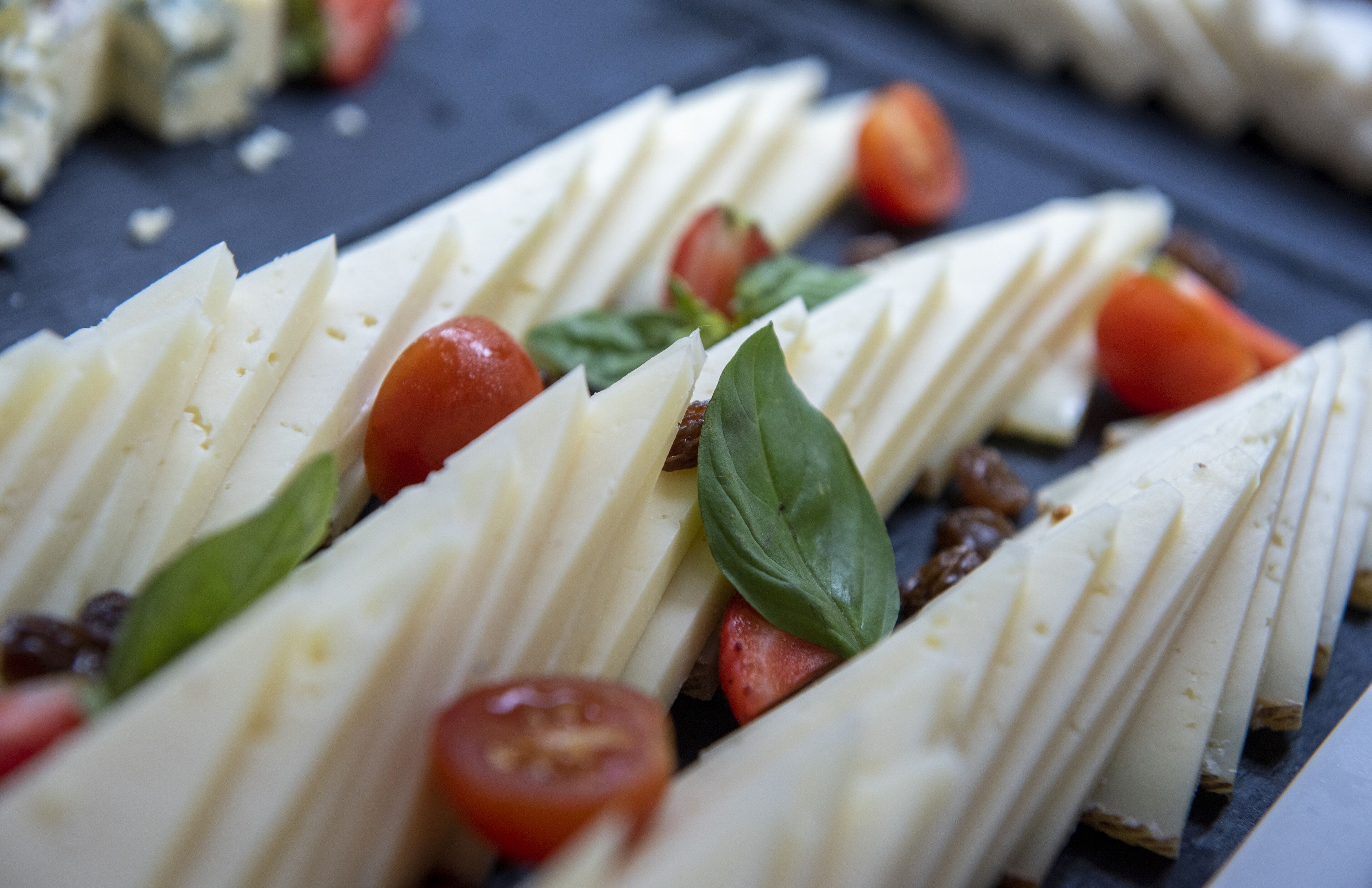 Nahaufnahme einer Käseplatte mit Käsescheiben, Cocktailtomaten und Basilikum.