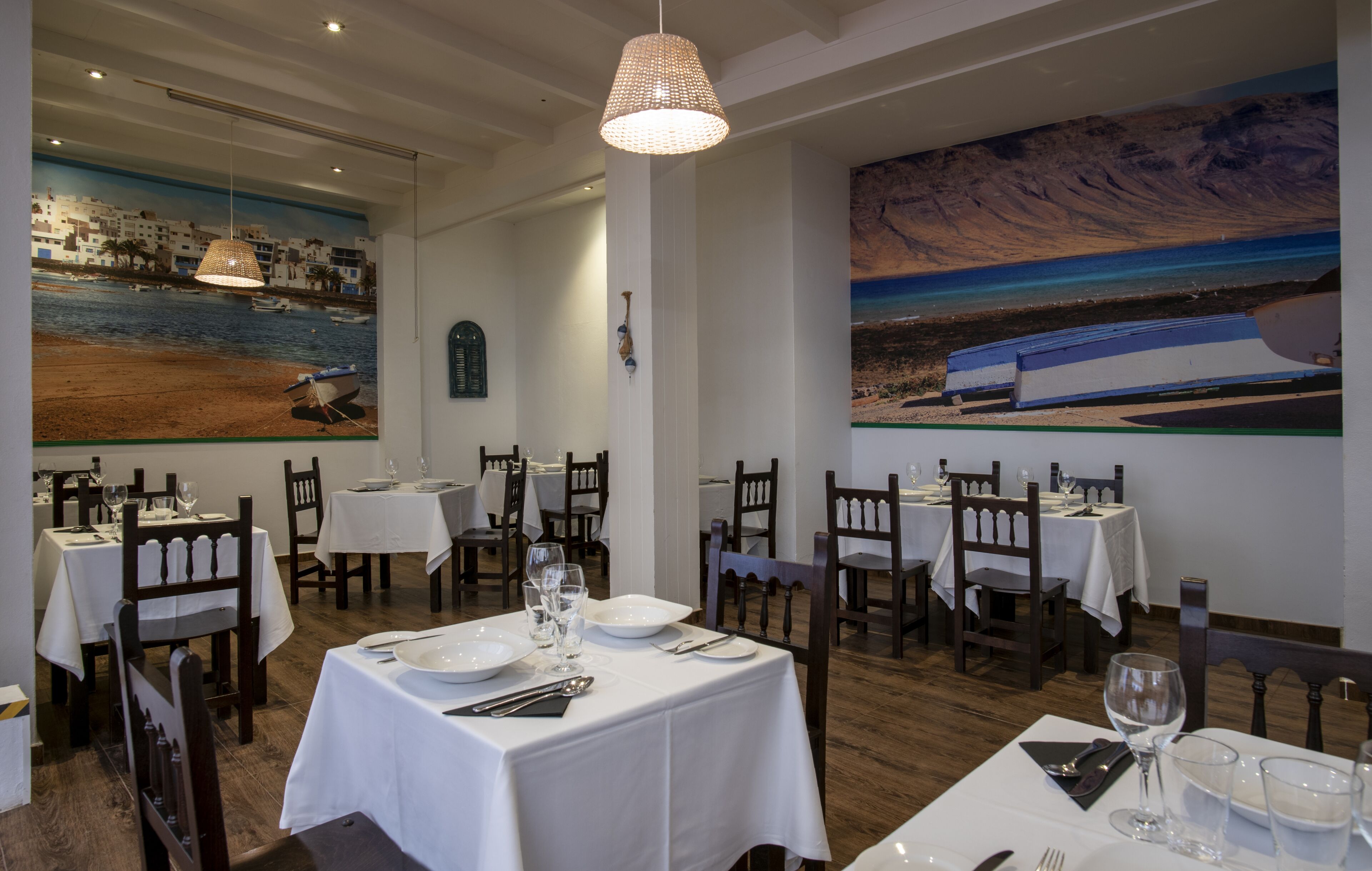Un restaurante con manteles blancos, sillas de madera y un cuadro grande de una escena costera.