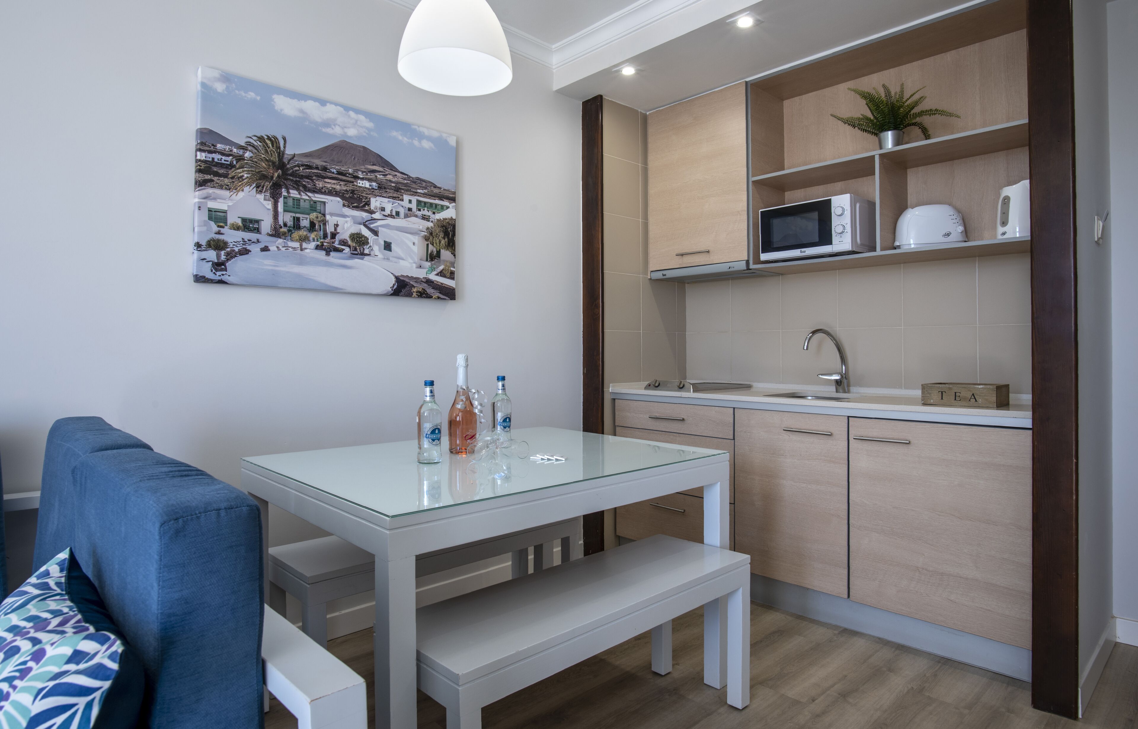 Una cocina compacta con una mesa de vidrio, un microondas y un lavamanos.
