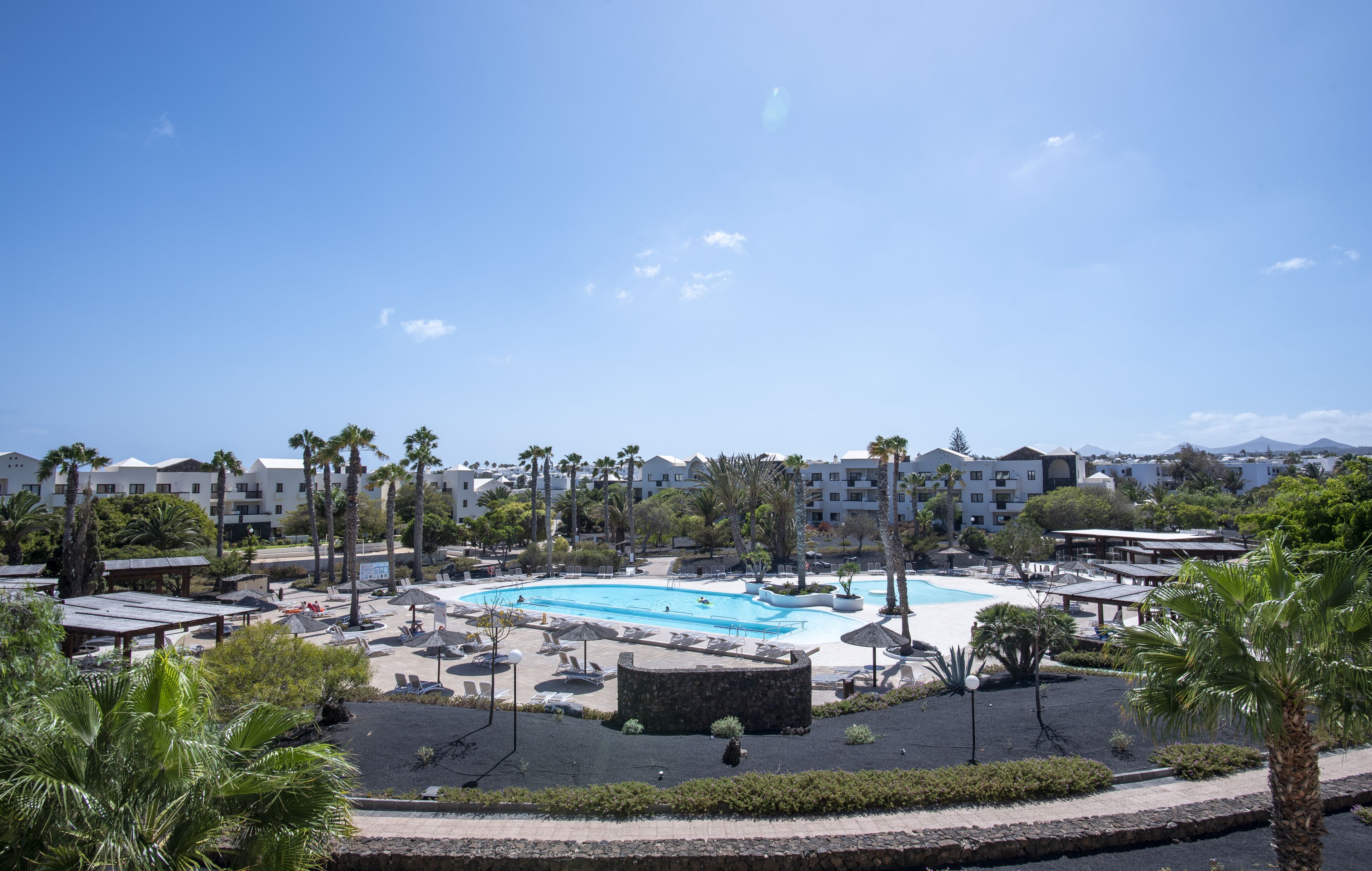 A resort with a large swimming pool, palm trees, and a clear blue sky.