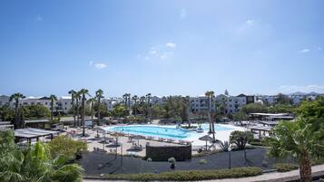 A resort with a large swimming pool, palm trees, and a clear blue sky.