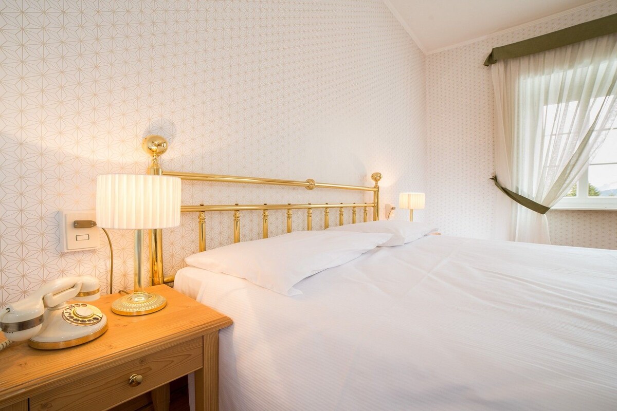 Une chambre d’hôtel avec un lit, une table de chevet avec une lampe, un téléphone et un mur recouvert d’un papier peint à motifs géométriques.