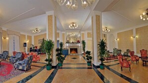 A spacious lobby with a central fireplace, multiple seating areas, and decorative plants. - TH San Martino | Majestic Dolomiti Hotel (Primiero San Martino di Castrozza)
