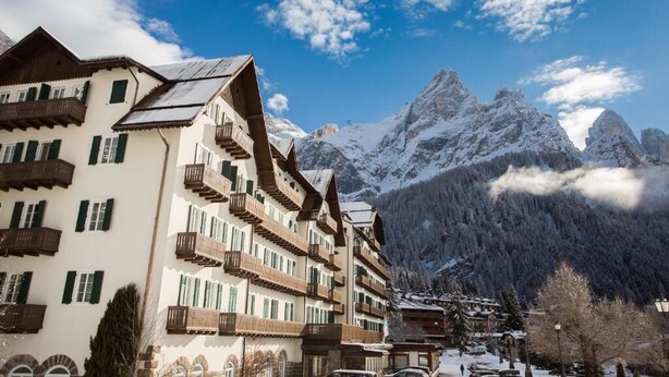 A multi-story hotel with balconies, a mountainous backdrop, and snow-covered peaks. - TH San Martino | Majestic Dolomiti Hotel (Primiero San Martino di Castrozza)