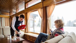 A cozy room with a wooden interior, a sofa, a table with a teapot and cups, and a window with curtains. - TH San Martino | Majestic Dolomiti Hotel (Primiero San Martino di Castrozza)