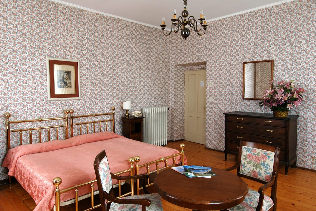 Ein Schlafzimmer mit einem Bett, einem Schminktisch, einem Sessel, einem Tisch, einem Spiegel und einer Deckenleuchte.
