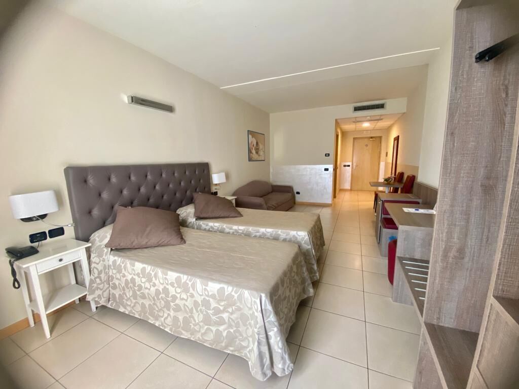 A hotel room with two beds, a small desk, and a kitchenette in the background.