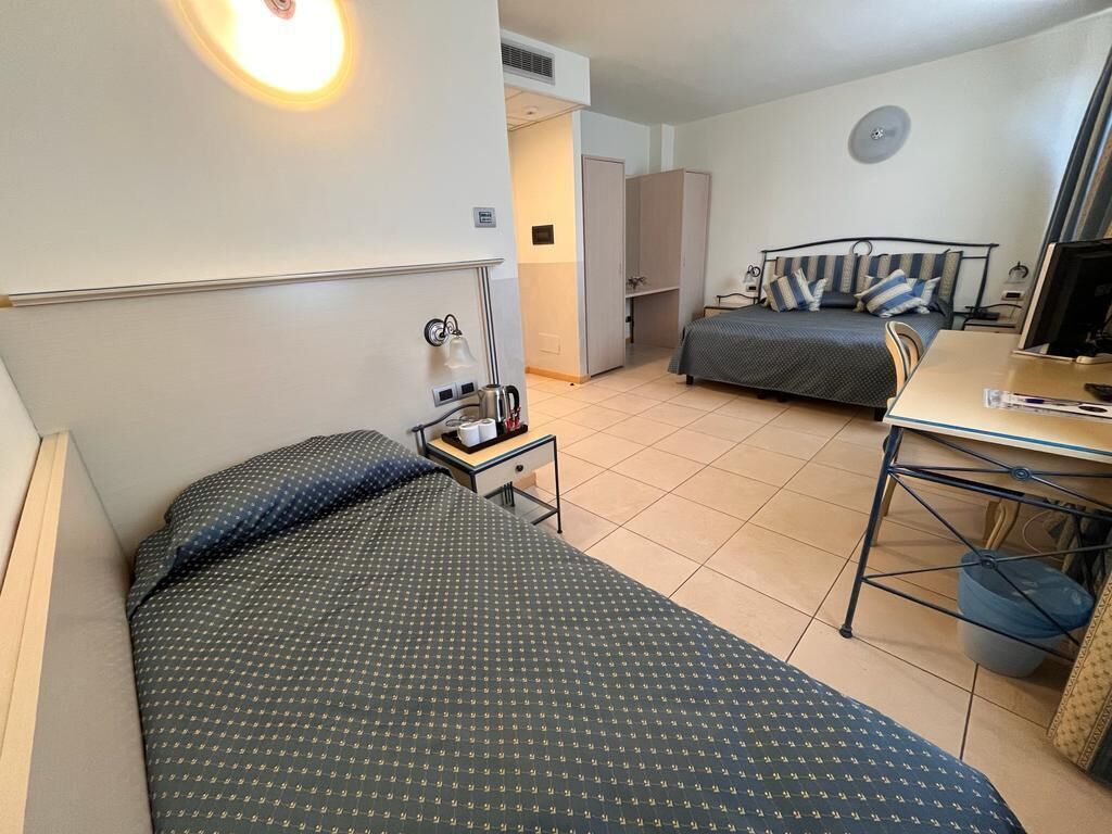 Hotelkamer met twee bedden, een bureau, een stoel, een tafeltje met een lamp en een prullenbak.