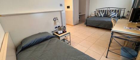 A hotel room with two beds, a desk, a chair, a small table with a lamp, and a trash bin.