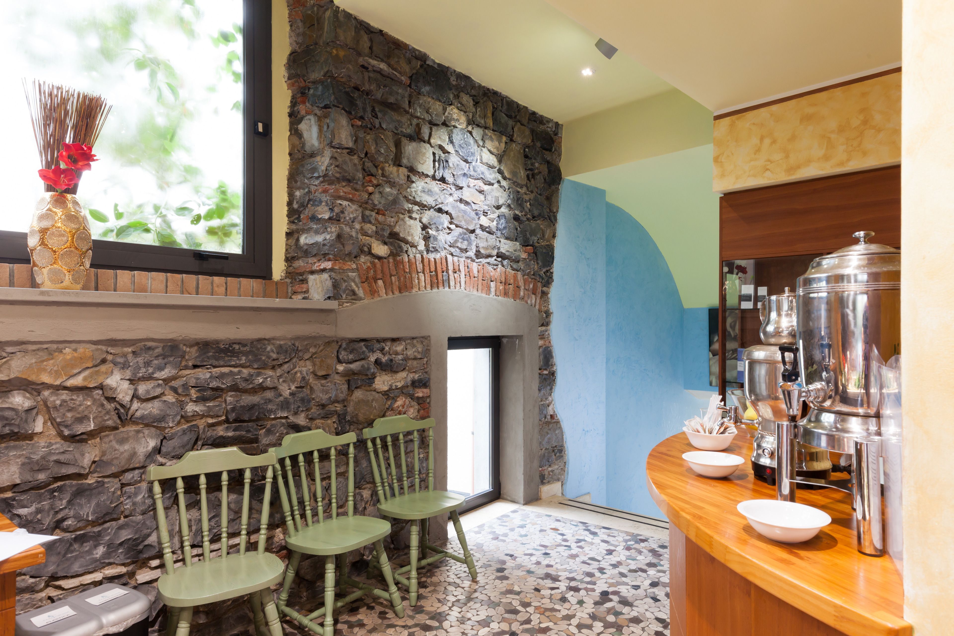 Un mur en pierre, des chaises en bois, un sol carrelé et un coin bar avec une machine à café.