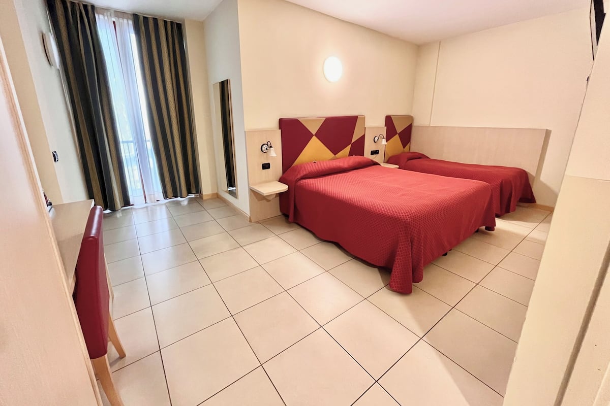 Ein Hotelzimmer mit zwei Betten, einem Nachttisch, einer Wandlampe und einem Fenster mit Vorhängen.