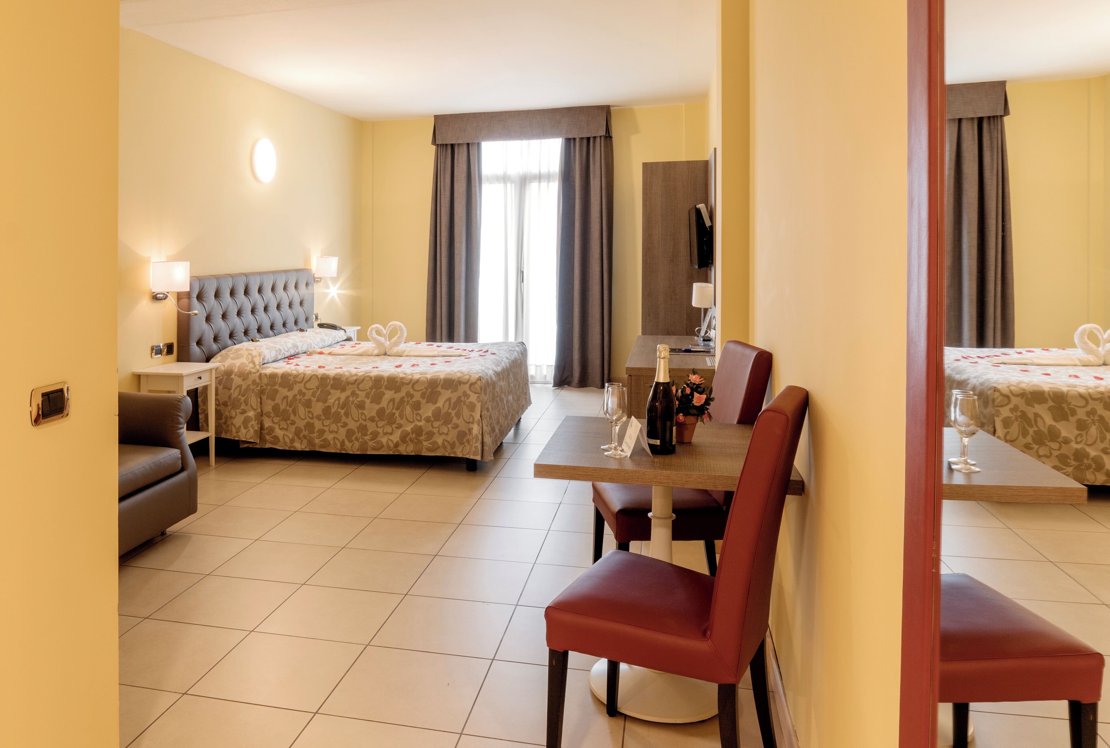A hotel room with two beds, a dining table with chairs, a sofa, a TV, and a mirror.