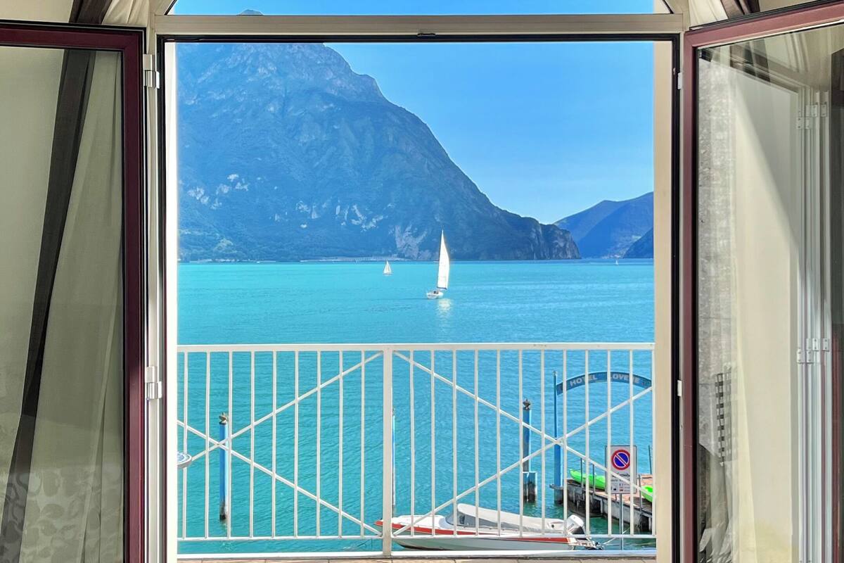 Blick von einem Balkon auf einen klaren Himmel, ein türkisfarbenes Meer und ferne Berge.