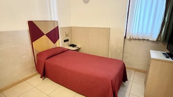 Una habitación de hotel con una cama individual, un escritorio y una ventana con cortinas.