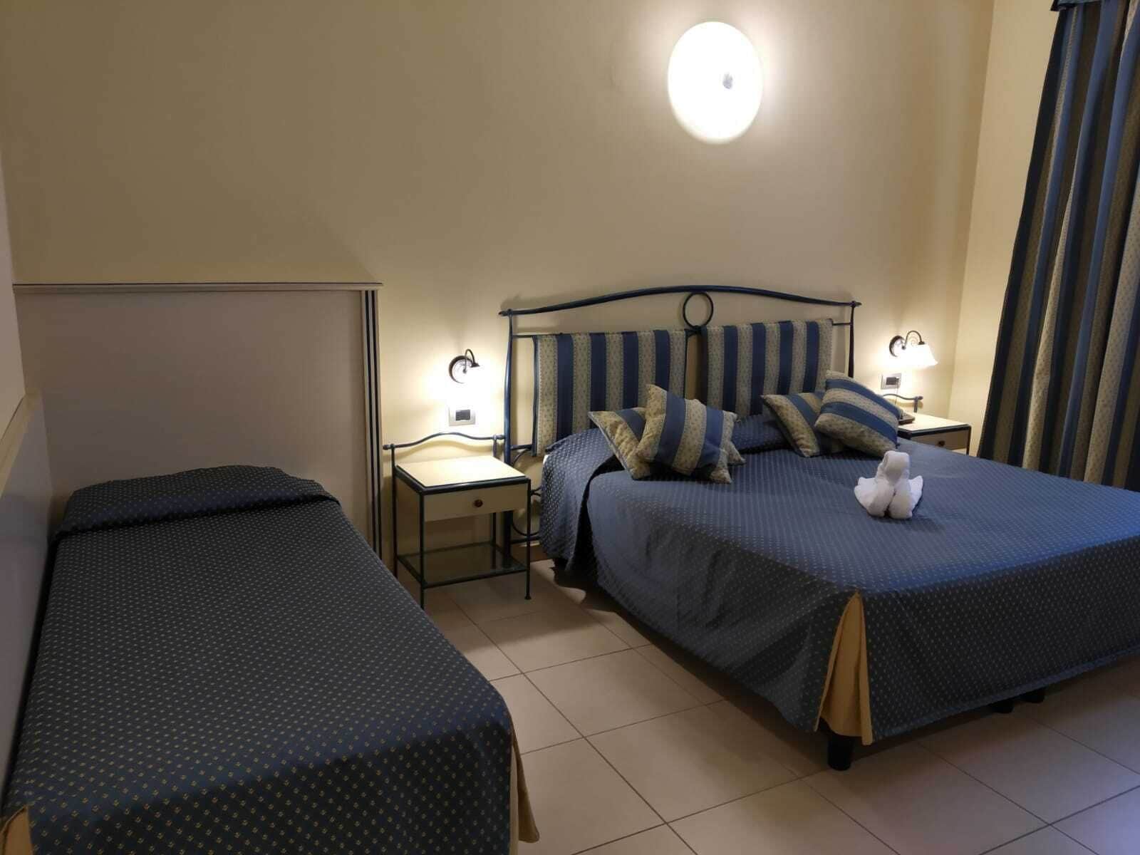 A hotel room with two single beds, a small desk, and a nightstand with a lamp.