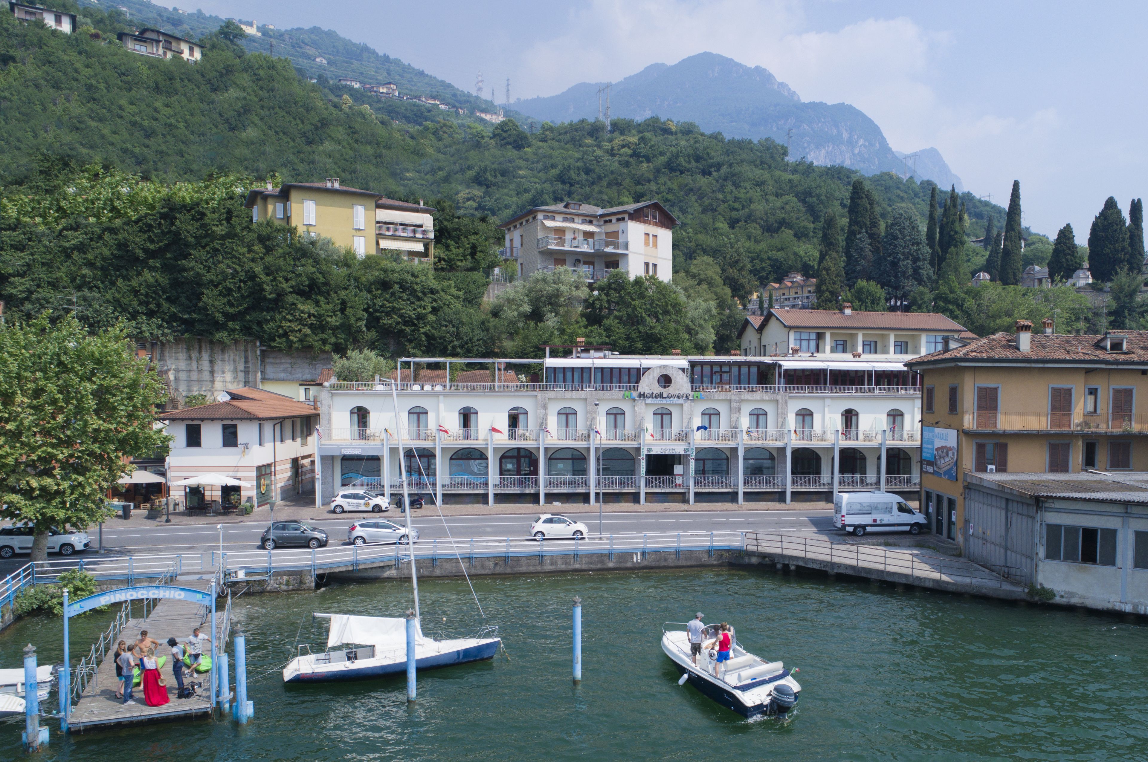 A waterfront hotel with multiple balconies, a dock with boats, and a road with cars.