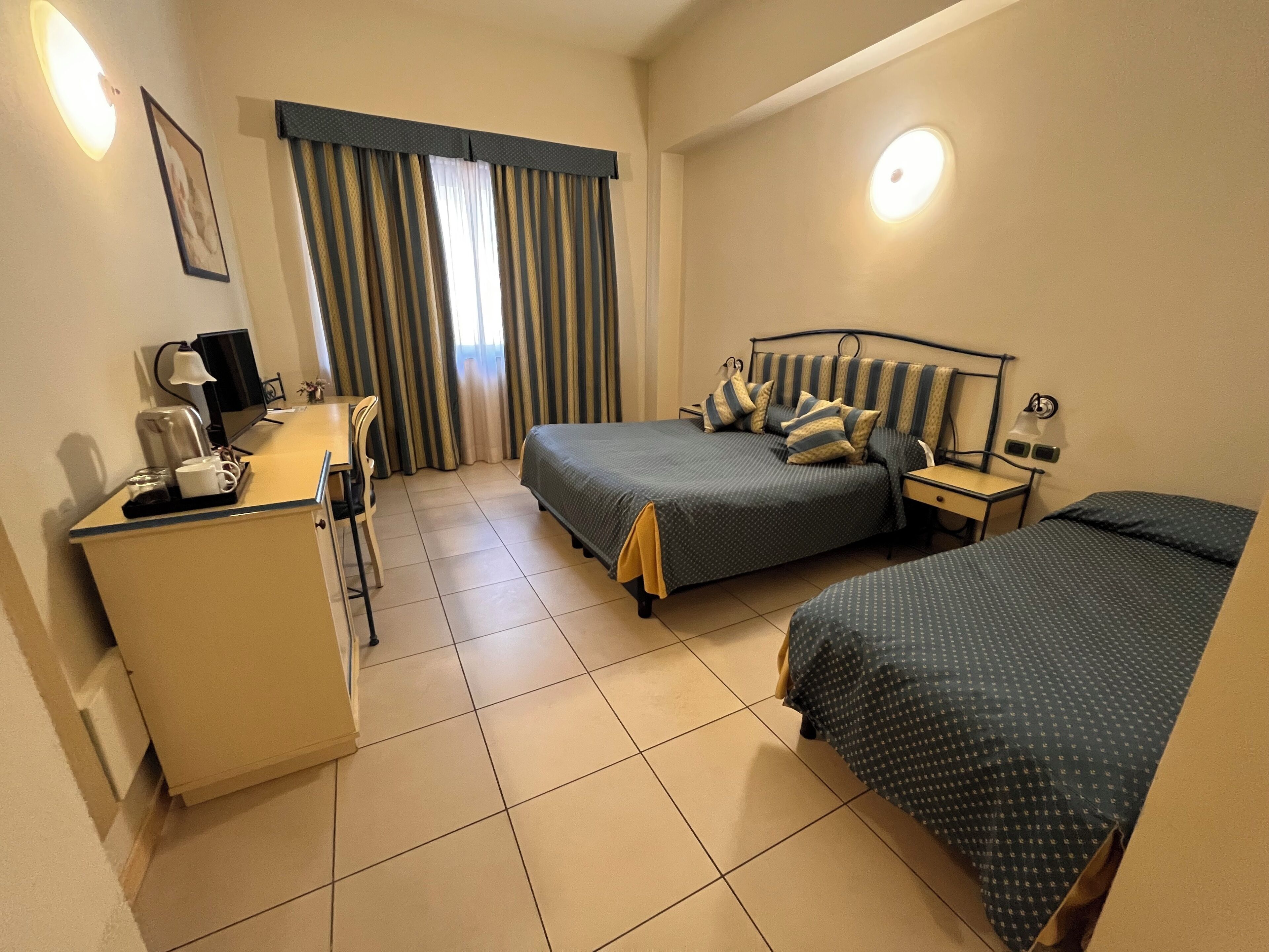 A hotel room with a bed, a desk, a chair, a TV, and a window with curtains.