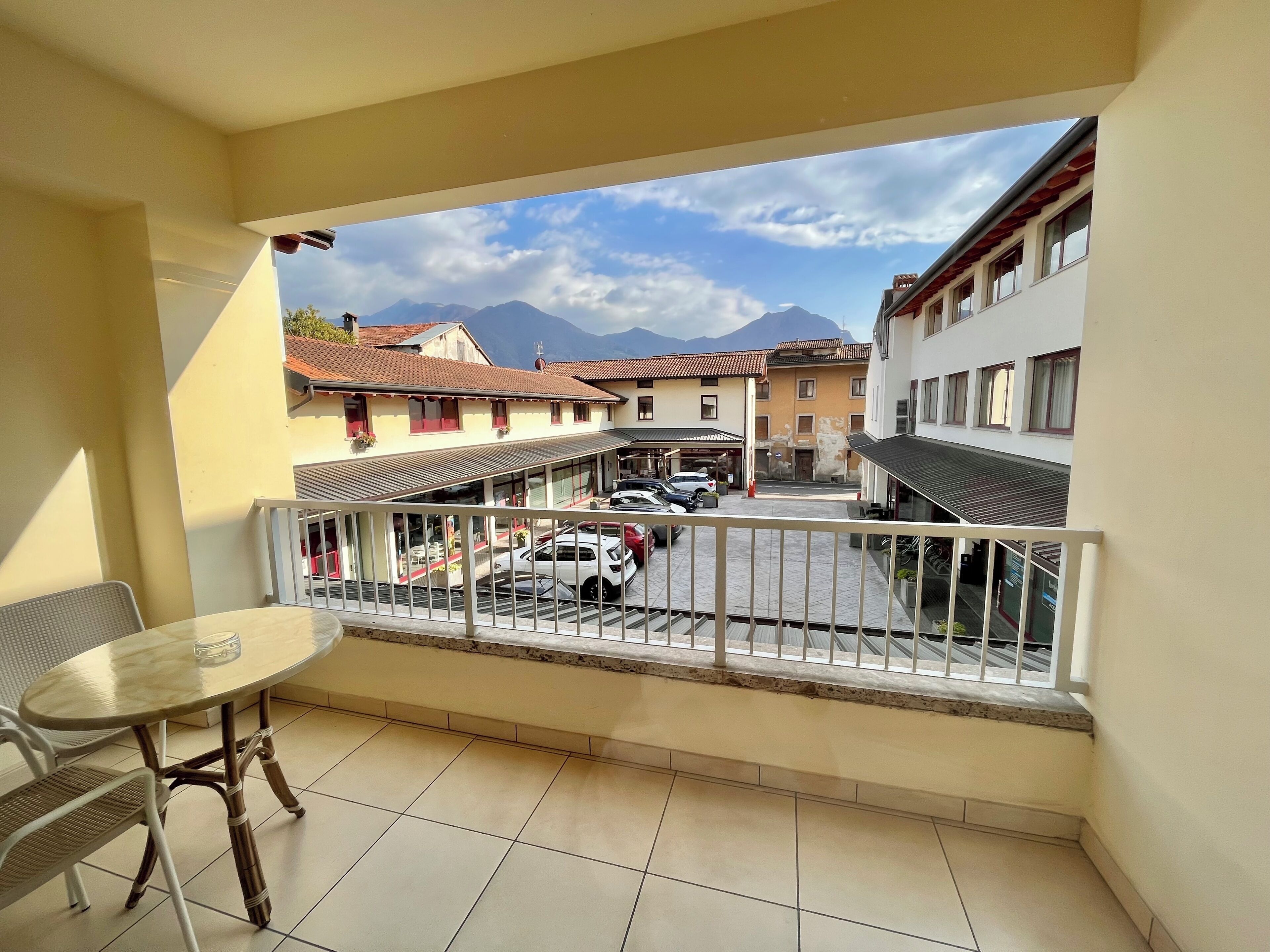 A balcony with a view of a street, a table, and chairs.