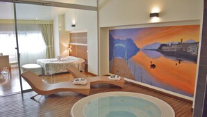 A hotel room with a large window, a bed, a lounge chair, a small table, and a painting of a sunset over a river. - Hotel Lovere Resort & Spa (Lovere)