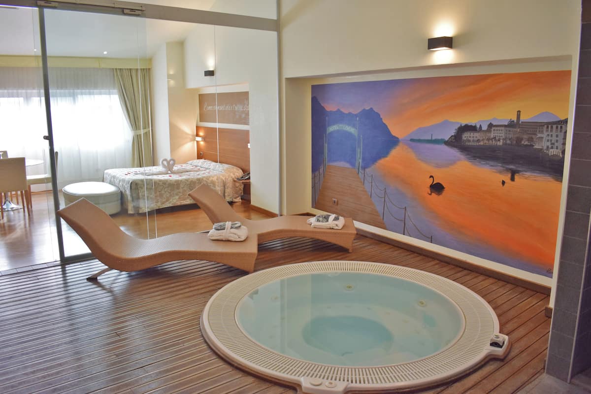 Ein Hotelzimmer mit großem Fenster, einem Bett, einem Sessel, einem kleinen Tisch und einem Gemälde mit einem Sonnenuntergang über einem Fluss.