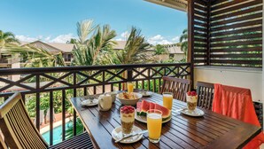 Une table en bois avec des aliments pour le petit-déjeuner, une piscine et une vue sur des maisons et des palmiers.