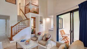 Un vaste espace de vie comprenant un escalier, une table à manger avec des chaises, un canapé et une vue à travers une porte vitrée.