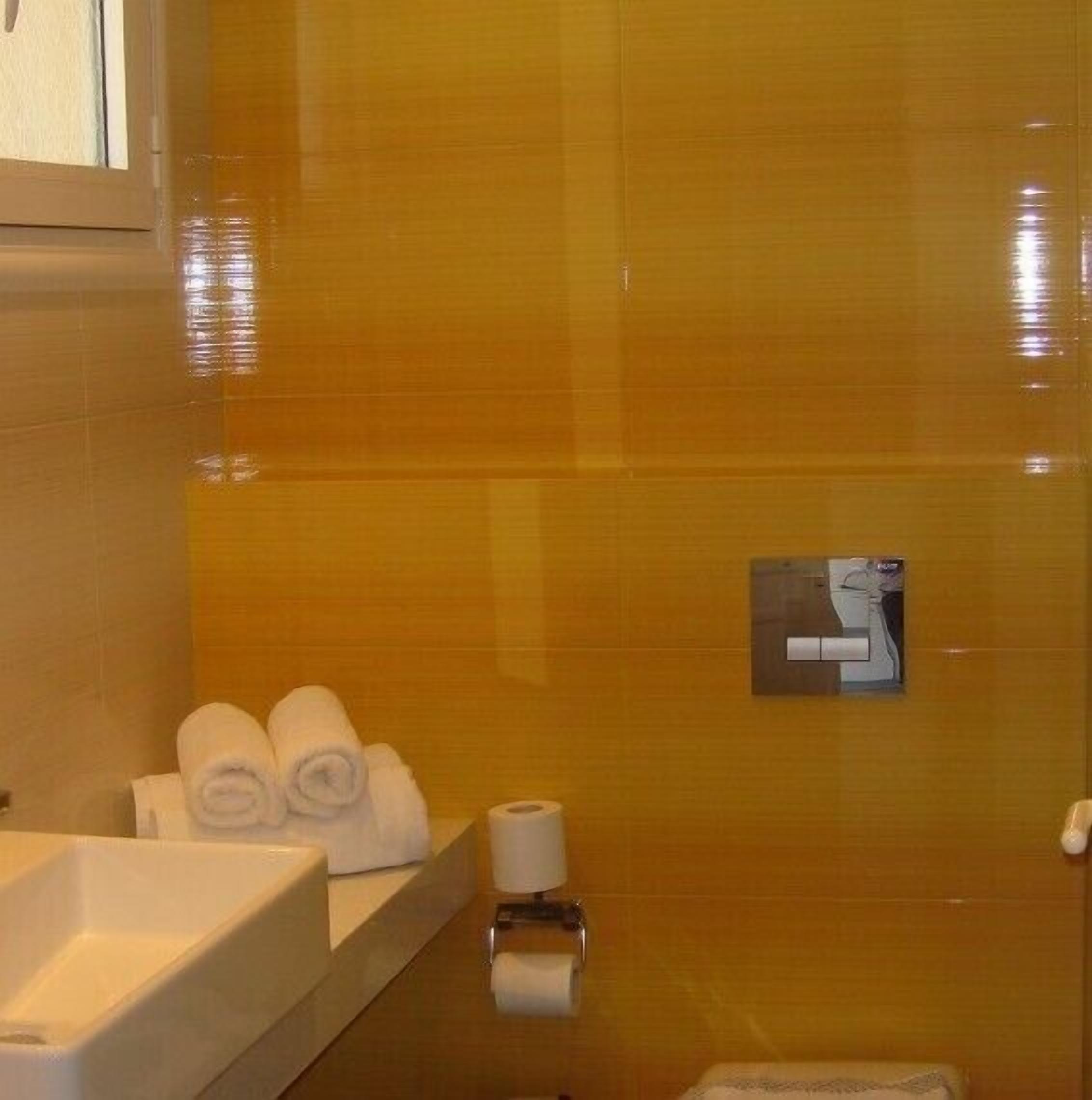 Un baño con pared de azulejos color beige, un lavamanos blanco y toallas ordenadas en una repisa.