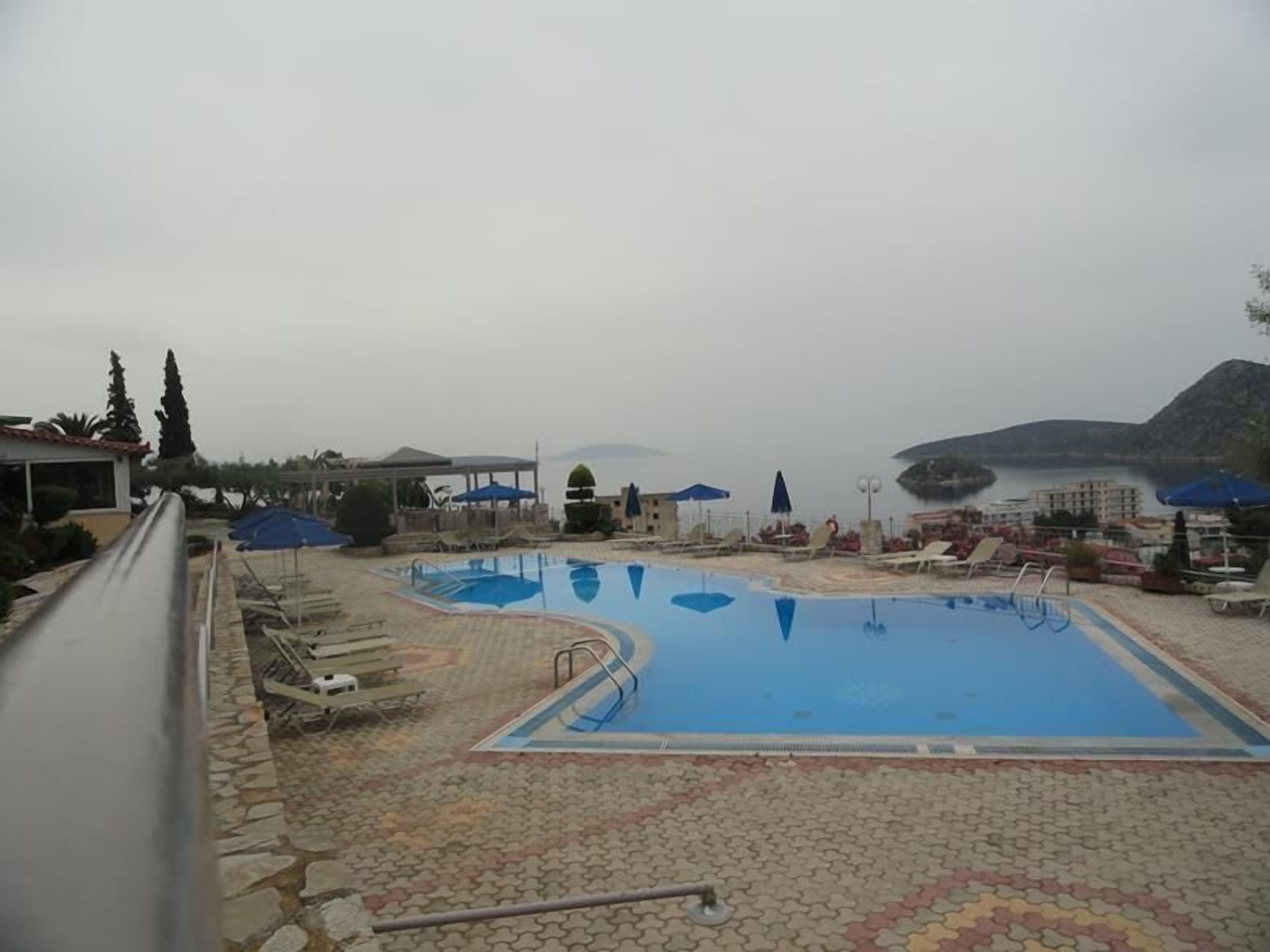 Une piscine entourée de bâtiments, dotée de chaises longues et de parasols, et offrant une vue sur la mer.