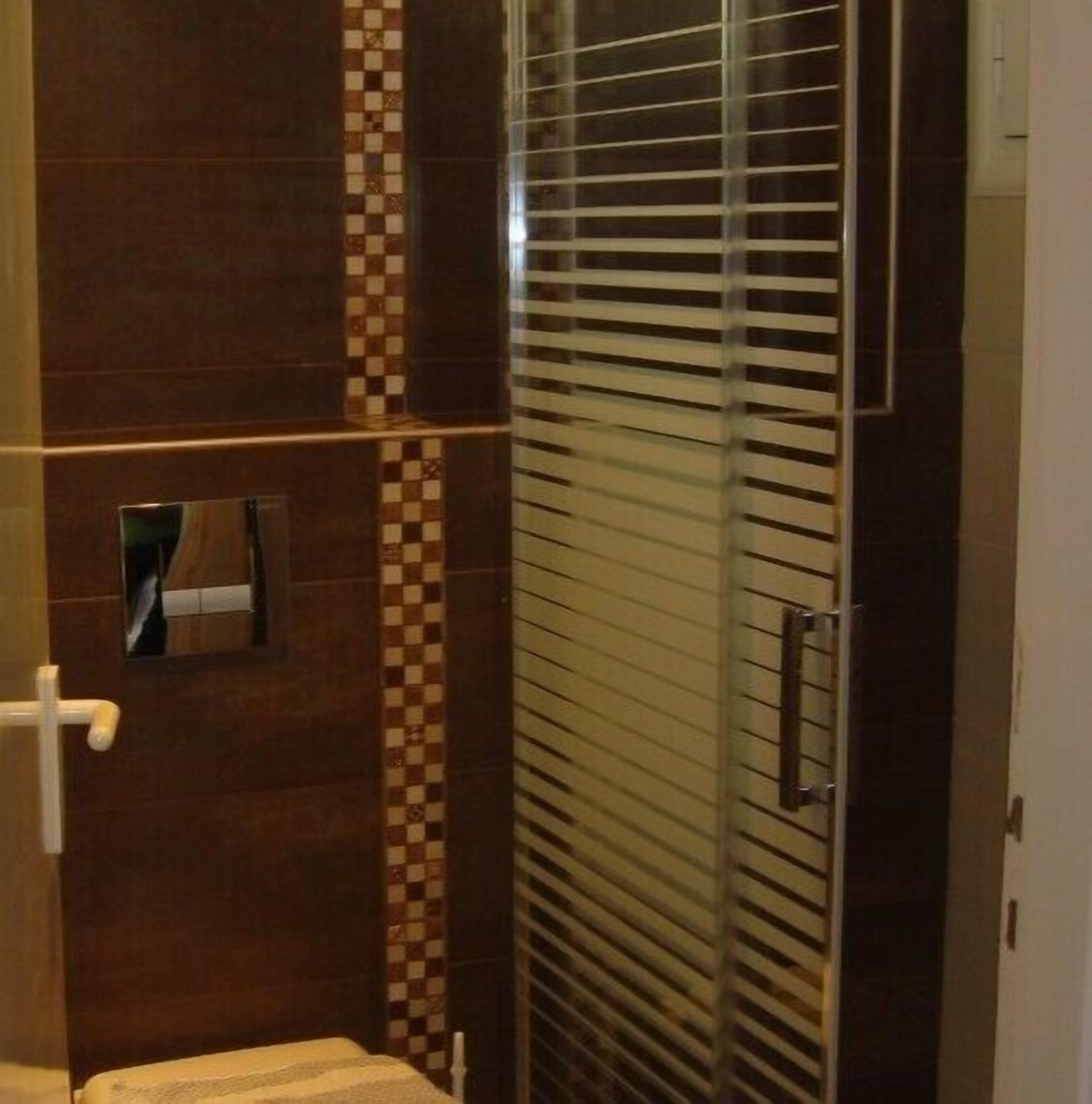 A bathroom with a glass shower enclosure, a towel rack, and a checkered tile backsplash.